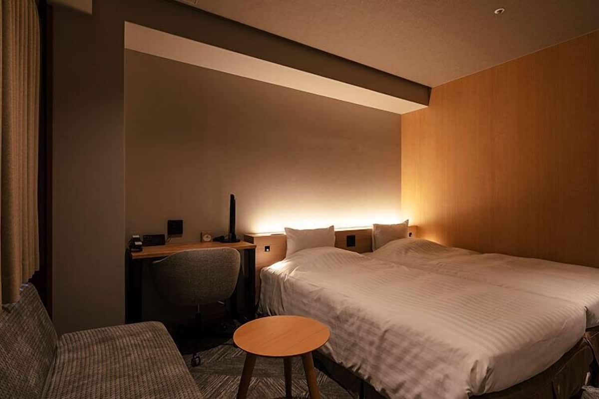 Ein Hotelzimmer mit zwei Betten, einem Schreibtisch, einem Stuhl und einem kleinen Tisch.