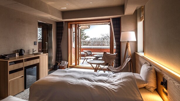Ein Hotelzimmer mit einem großen Bett, einem Schreibtisch mit Wasserkocher, einem Stuhl und Blick ins Freie.