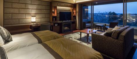 Una habitación de hotel moderna con dos camas grandes, un televisor de pantalla plana, una chimenea, un balcón con vistas y una zona de estar con mesa y sillas.