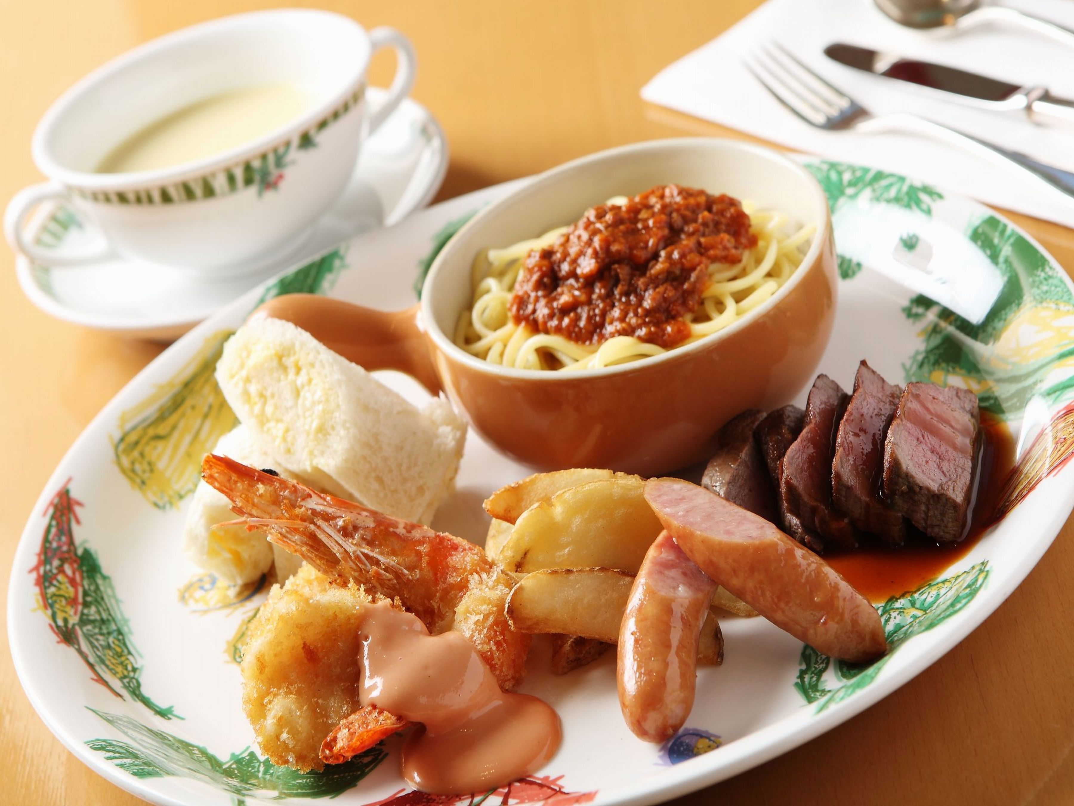 A plate with various foods including shrimp, sausage, and beef, along with a bowl of spaghetti and a cup of soup.