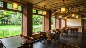 Ein großzügiges Restaurant mit Backsteinwänden, großen Fenstern mit Blick auf einen grünen Garten und mehreren Holztischen und Stühlen.