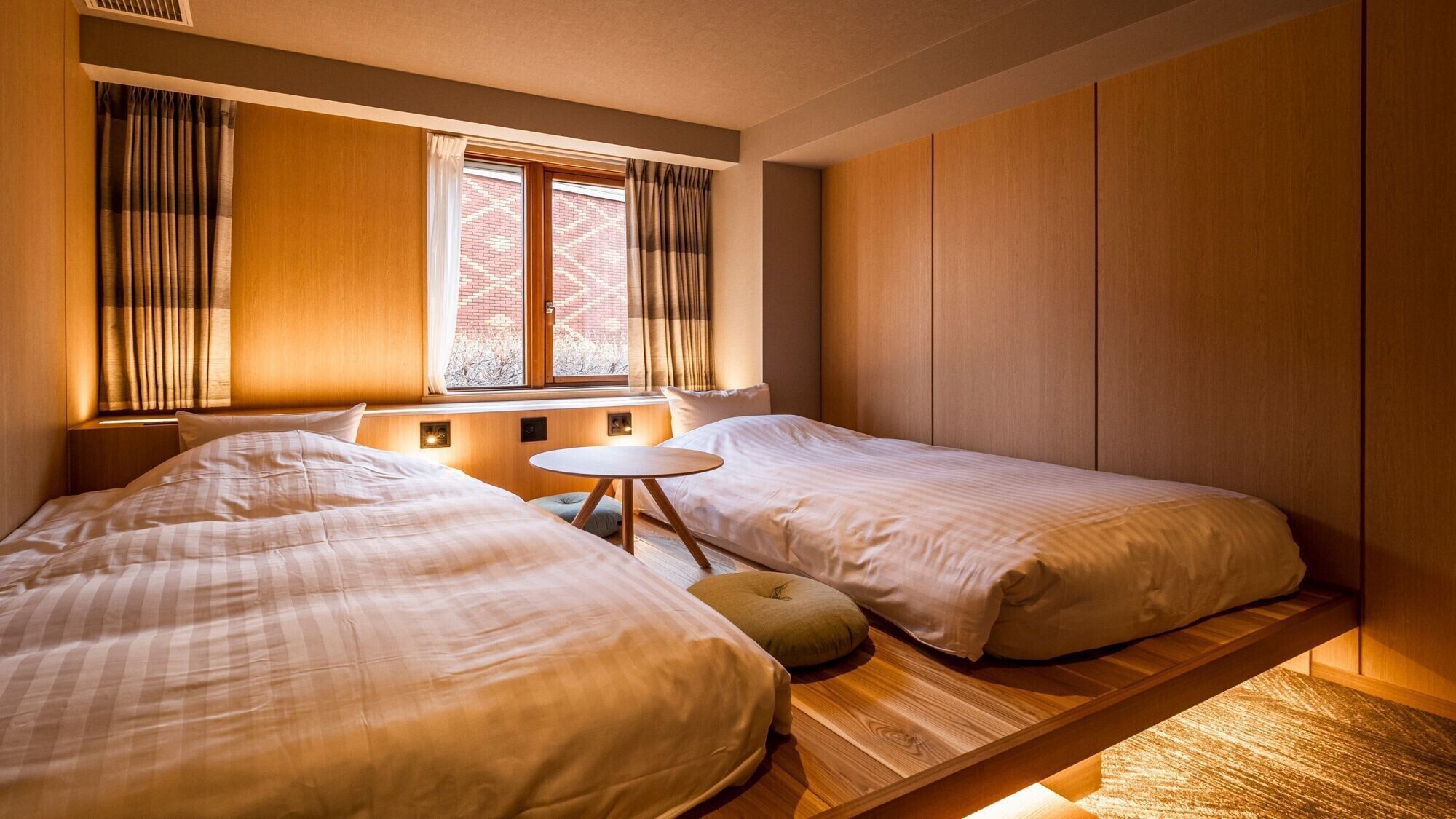 A hotel room with two beds, a small round table, and a window with curtains.