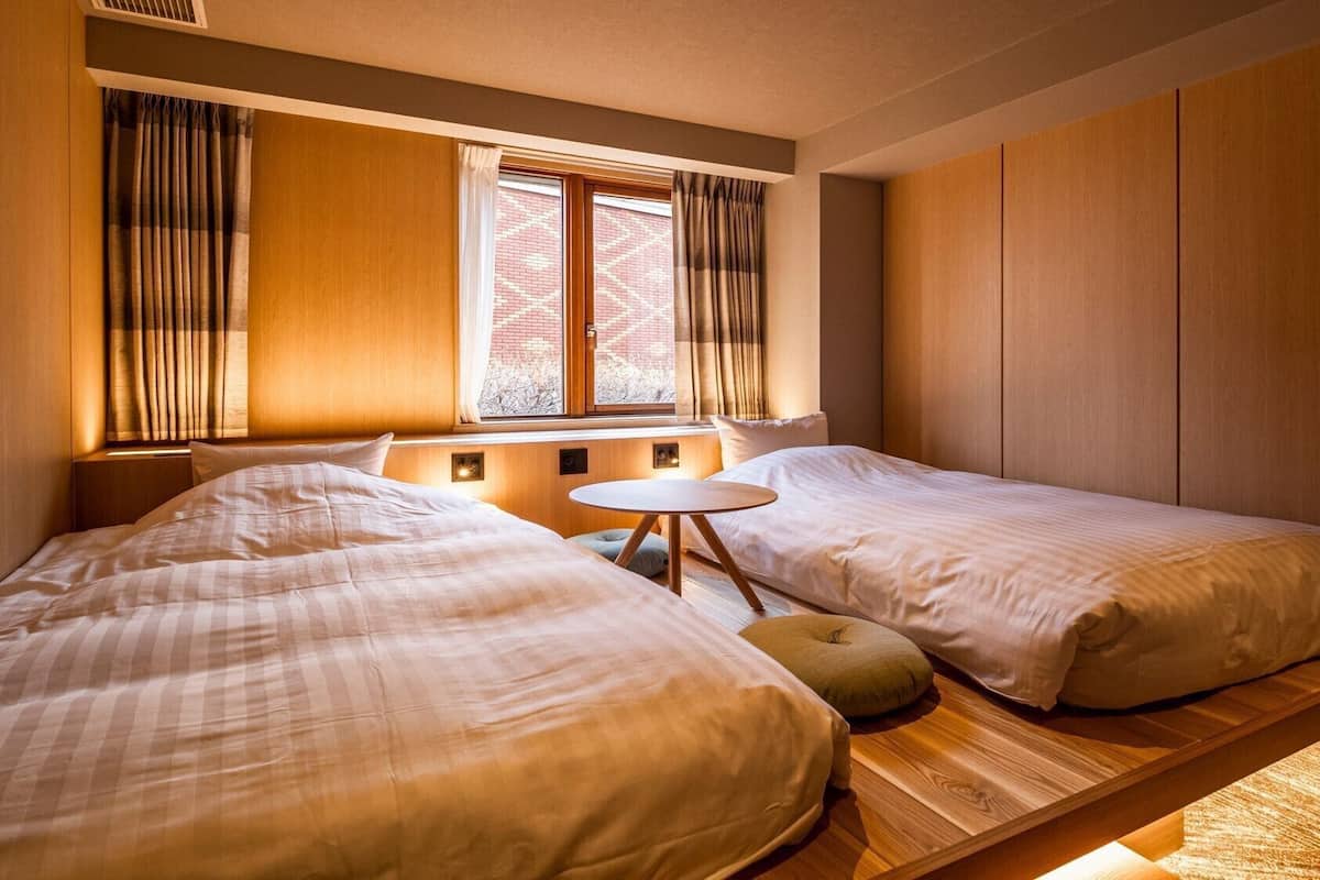 Ein Hotelzimmer mit zwei Betten, einem kleinen runden Tisch und einem Fenster mit Vorhängen.