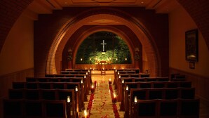 Ein gewölbter Innenraum mit in Reihen angeordneten Kirchenbänken, einem zentralen Gang mit Kerzen und einem Kruzifix am Altar.