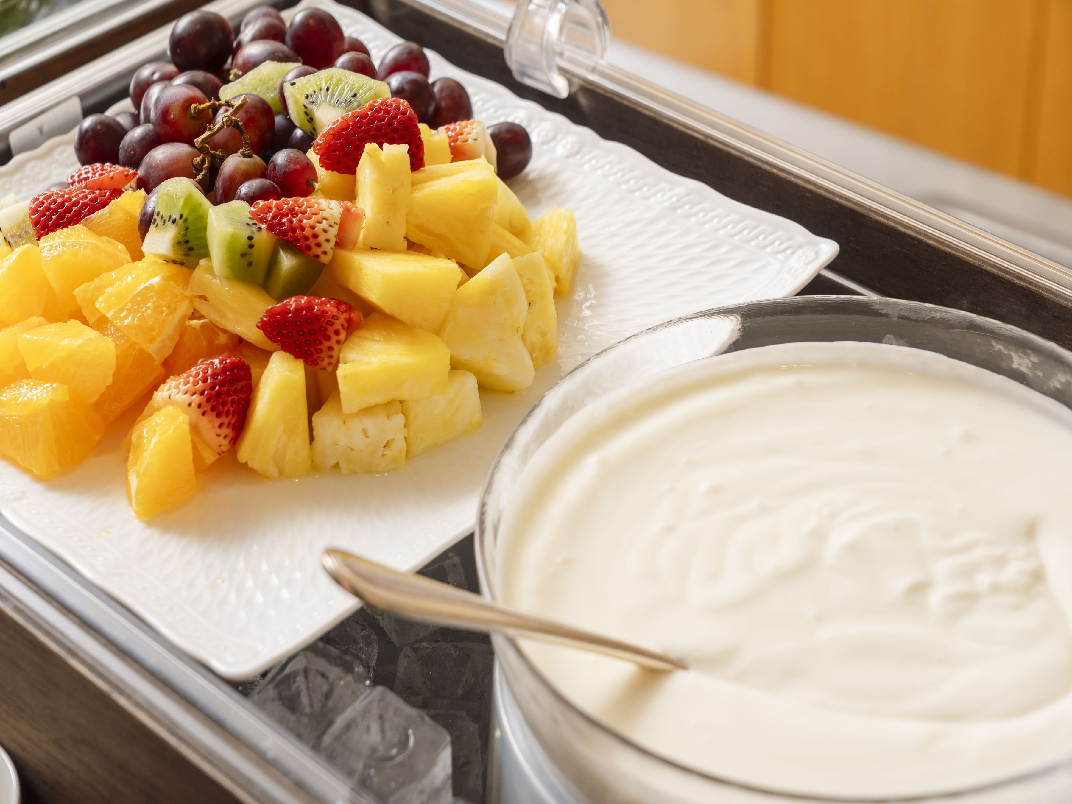 A tray with a variety of fruits and a bowl of white creamy substance, possibly yogurt or ice cream.