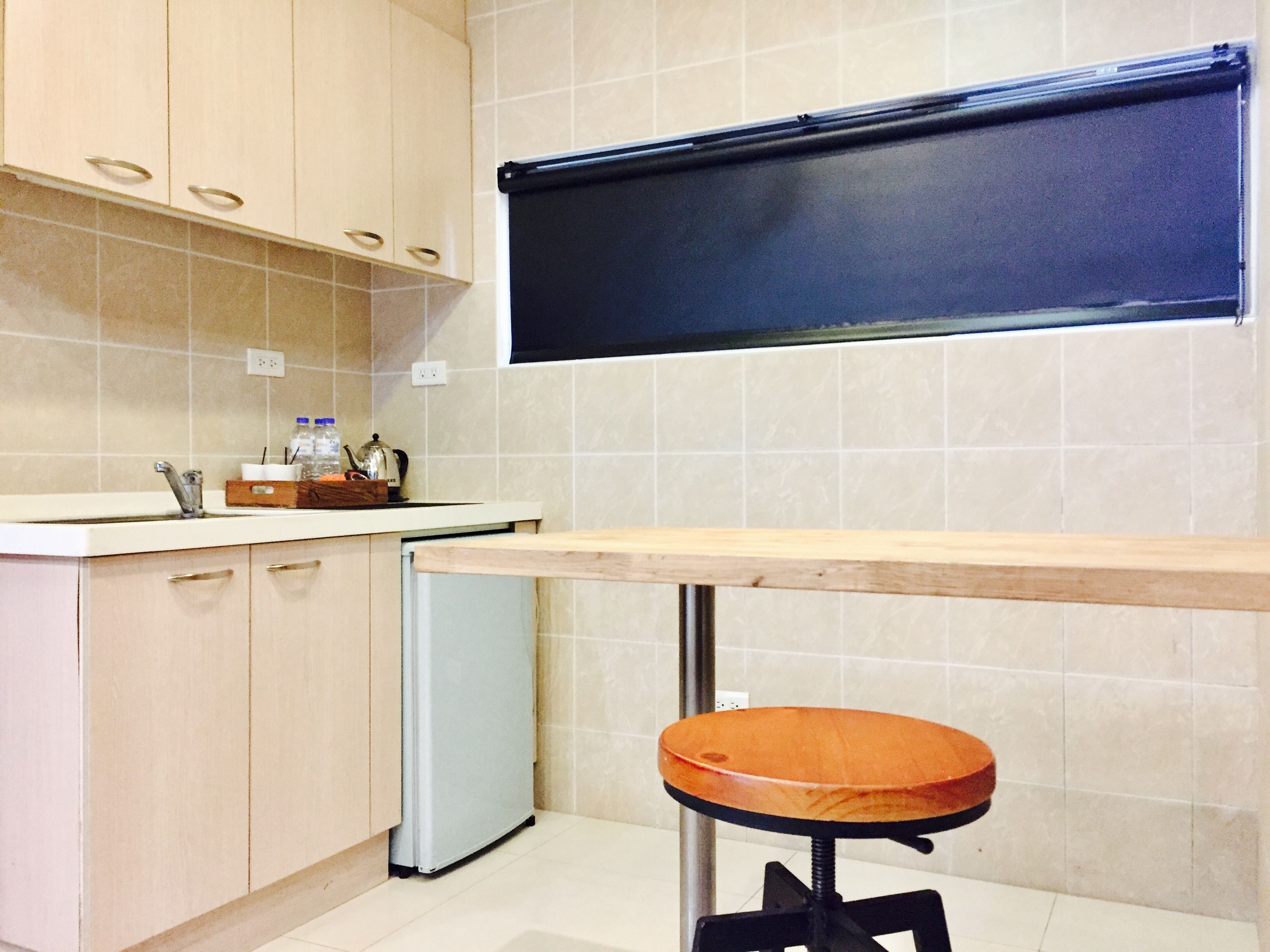 A kitchen with a wooden countertop, a sink, cabinets, a refrigerator, and a window above the countertop.