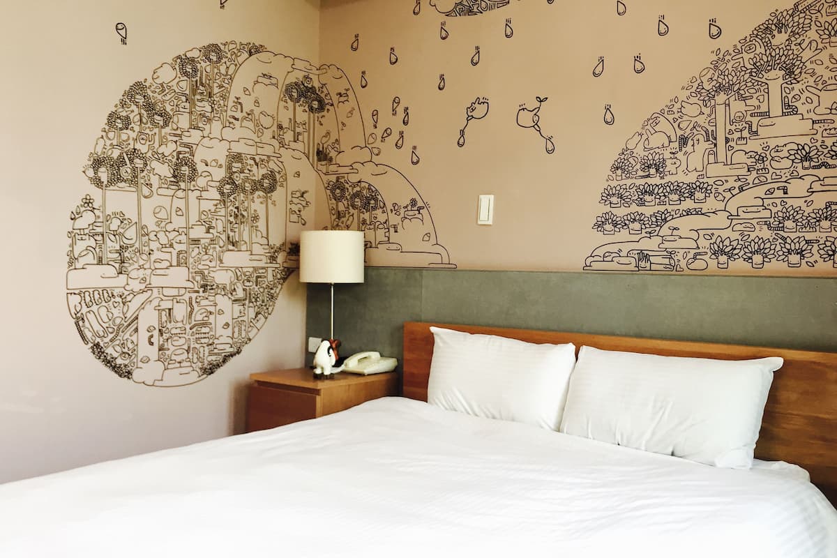 Une chambre d’hôtel avec un lit, une table de chevet avec une lampe et un mur orné d’une fresque.
