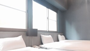 Una habitación de hotel con una cama grande, una mesita de noche con lámpara y un ventanal que deja entrar luz natural.