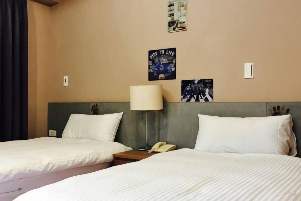 Une chambre d’hôtel avec deux lits, une table de chevet avec une lampe et une affiche au mur.