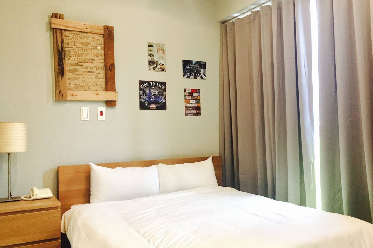 Une chambre d’hôtel avec un lit, une table de chevet, une lampe et un mur orné de divers affiches.