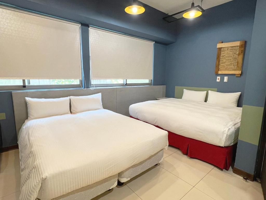 A hotel room with two beds, a window with blinds, a wall-mounted light fixture, and a wooden plaque.