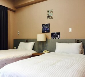 A hotel room with two beds, a bedside lamp, a telephone, and wall art.