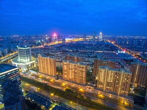 Une vue nocturne d’une ville, avec de hauts immeubles, des rues illuminées et une tour imposante surmontée d’une lumière rouge.