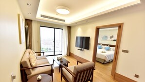A modern hotel room with a sofa, armchair, small table, and a TV on the wall. - Green Court Place Jinqiao Middle Ring Shanghai (Shanghai)