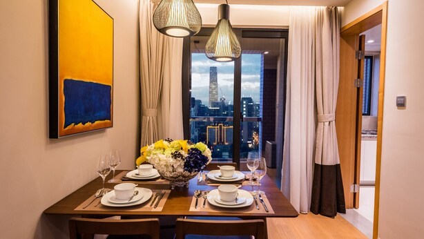 A dining area with a table set for two, a vase of flowers, and a cityscape view through the window. - Green Court Place Jinqiao Middle Ring Shanghai (Shanghai)