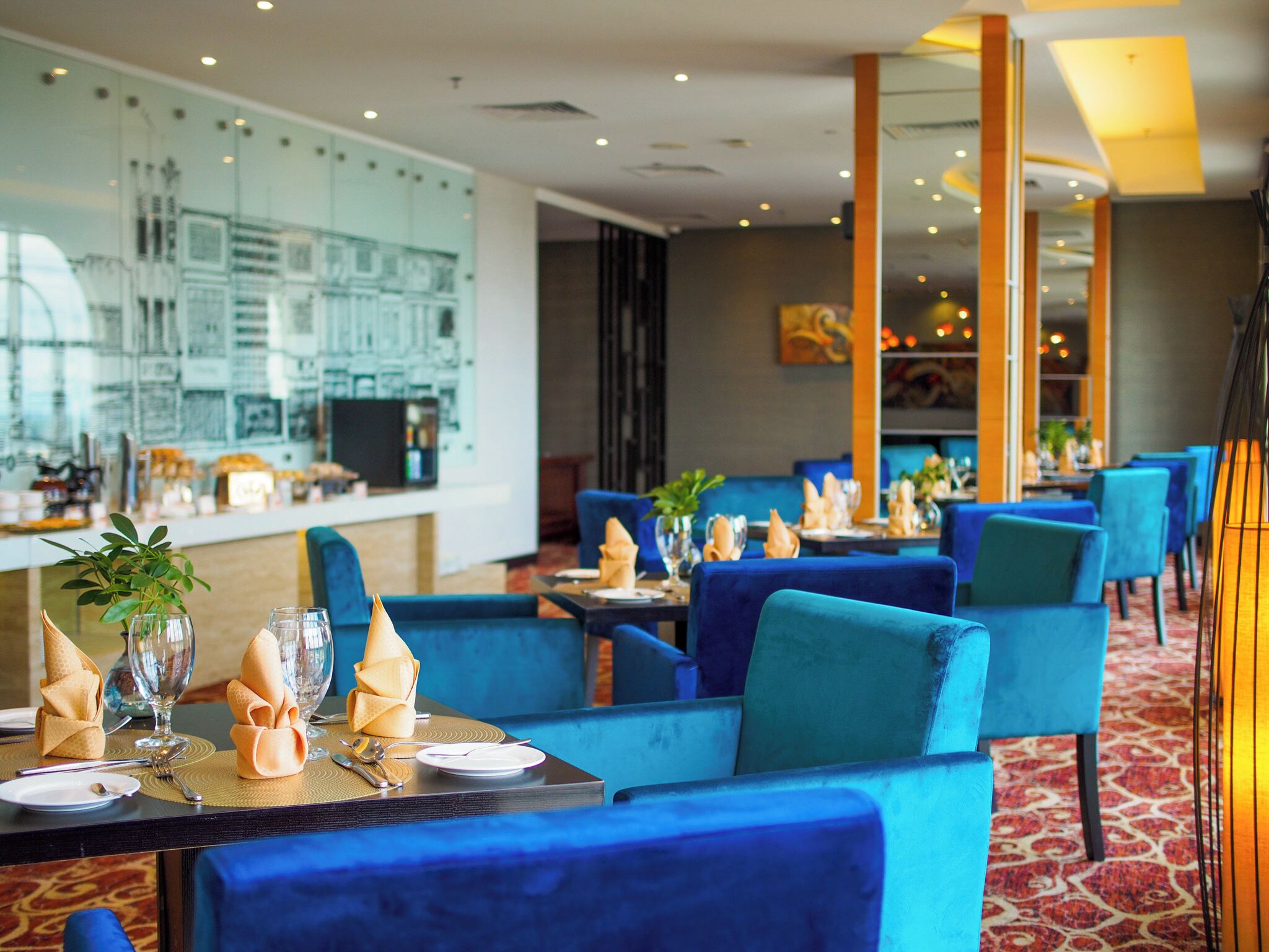 A restaurant with blue upholstered chairs, neatly set tables with folded napkins, and a patterned carpet.
