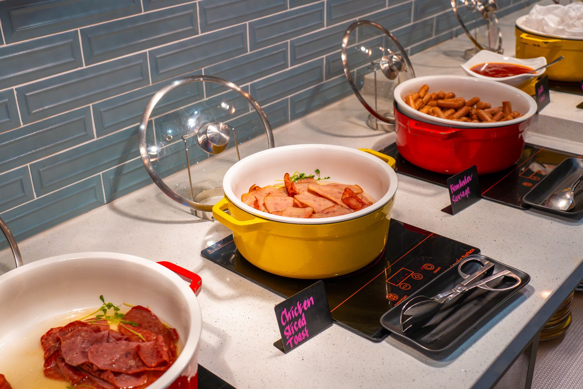 A buffet with various dishes including a yellow pot of sliced chicken, a red pot of fries, and a white bowl of sliced meat.