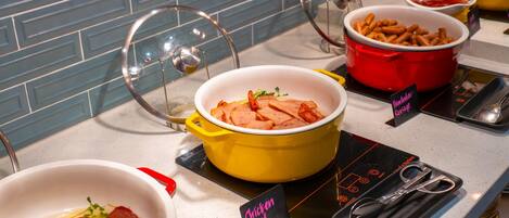 Un buffet con diversi piatti, tra cui una pentola gialla con pollo a fette, una pentola rossa con patatine fritte e una ciotola bianca con carne a fette.