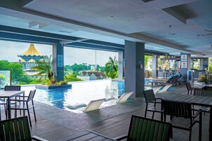 Zona de piscina con sillones y mesas, vista de un edificio con tejado amarillo y un letrero que indica prohibido fumar.