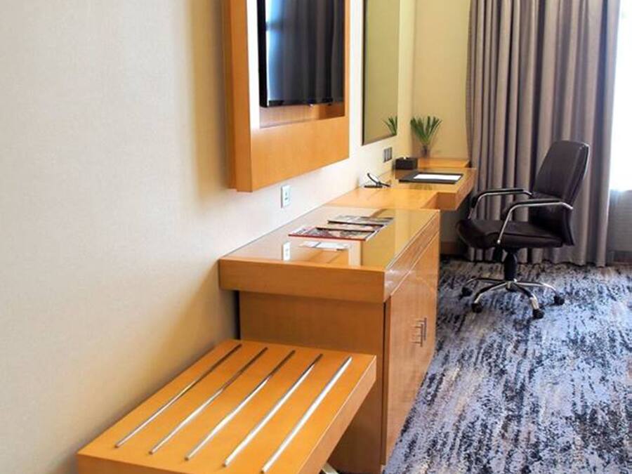 Habitación de hotel con un escritorio de madera, televisor montado en la pared, una silla y piso alfombrado.