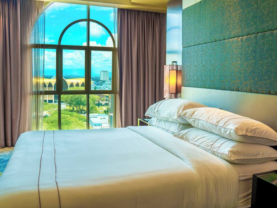 A hotel room with a large bed, a view of a cityscape through a window, and a modern headboard.