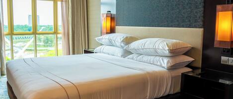 A hotel room with a large bed, two bedside lamps, a view of a cityscape, and a window with curtains.