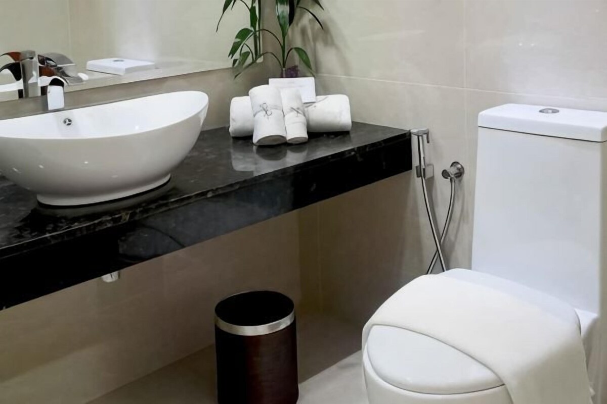 A bathroom with a white sink, a toilet, a trash can, and a plant.