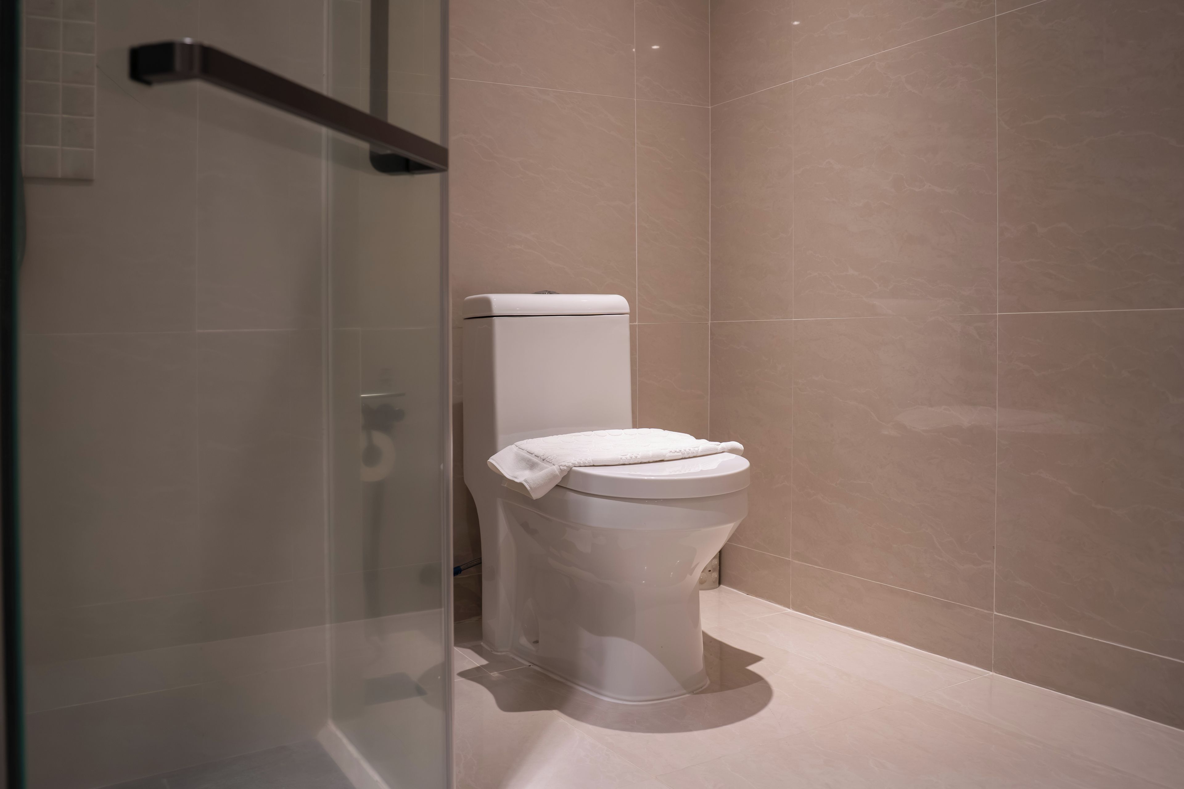 A modern bathroom with a toilet, a glass shower enclosure, and beige tiled walls.