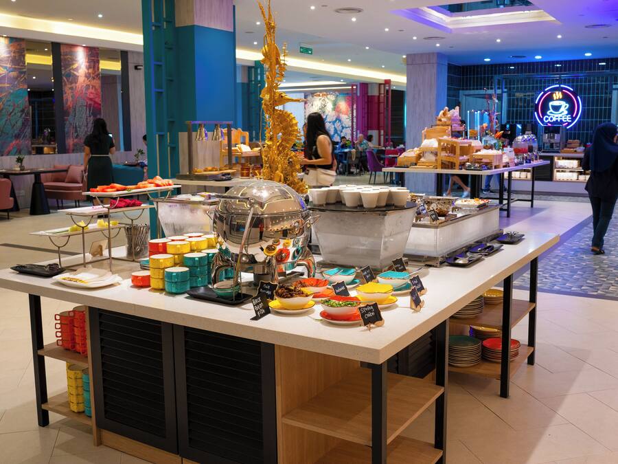 A buffet setup with various food items and a coffee station in a modern hotel lobby.