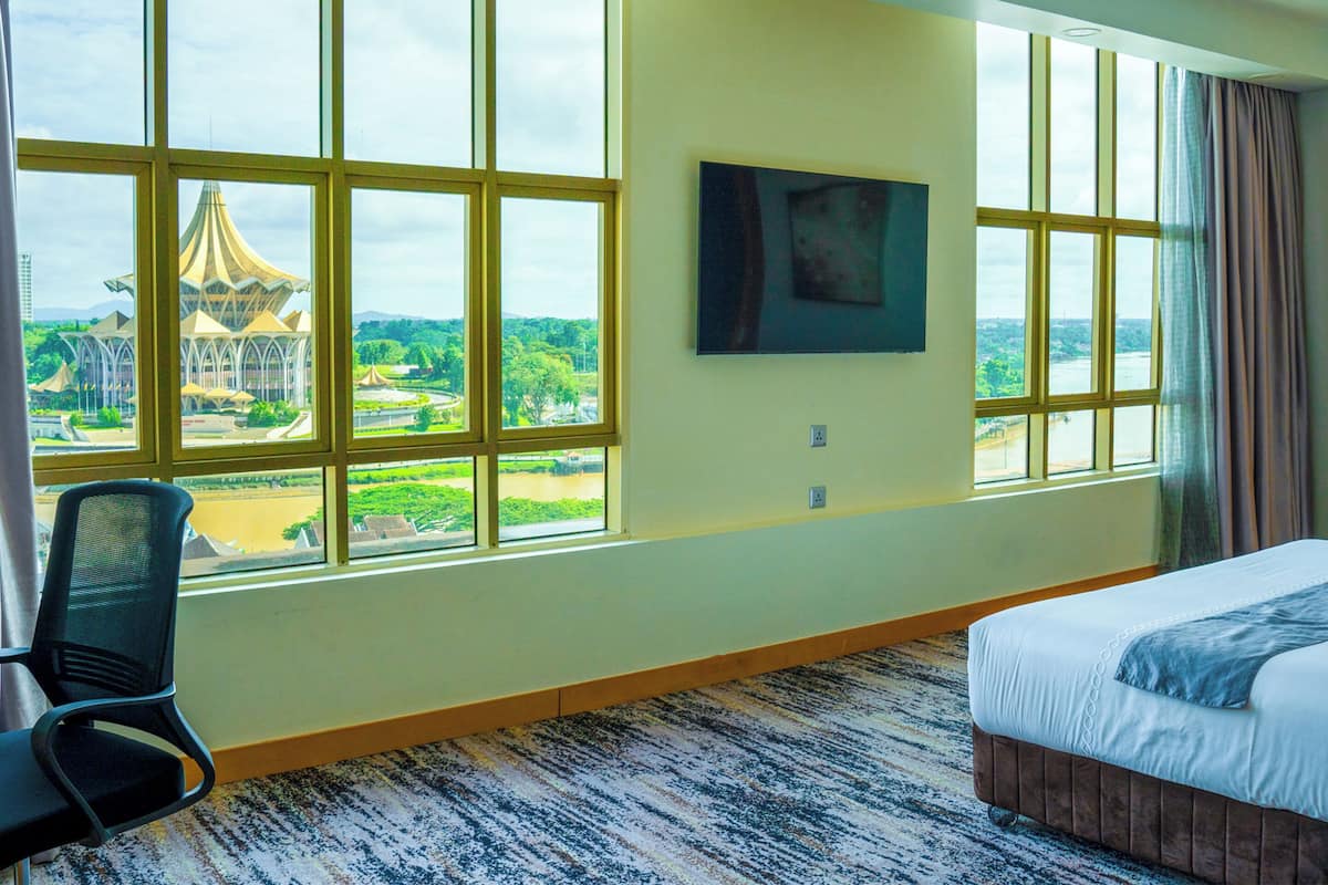 A hotel room with large windows, a bed, a chair, and a painting on the wall.