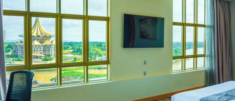 A hotel room with large windows, a bed, a chair, and a painting on the wall.