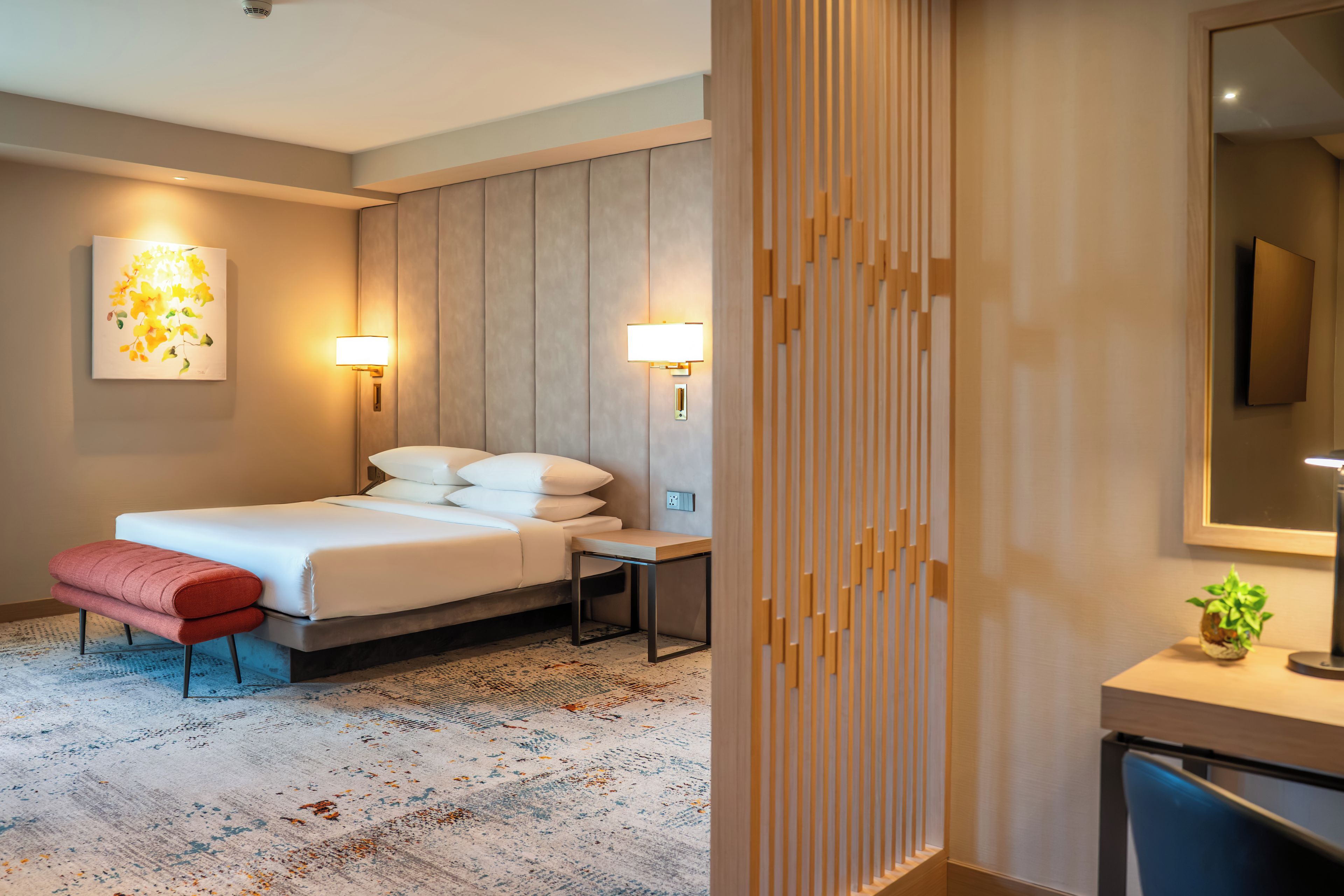 A hotel room with a bed, bedside table, lamp, and a wall-mounted TV.