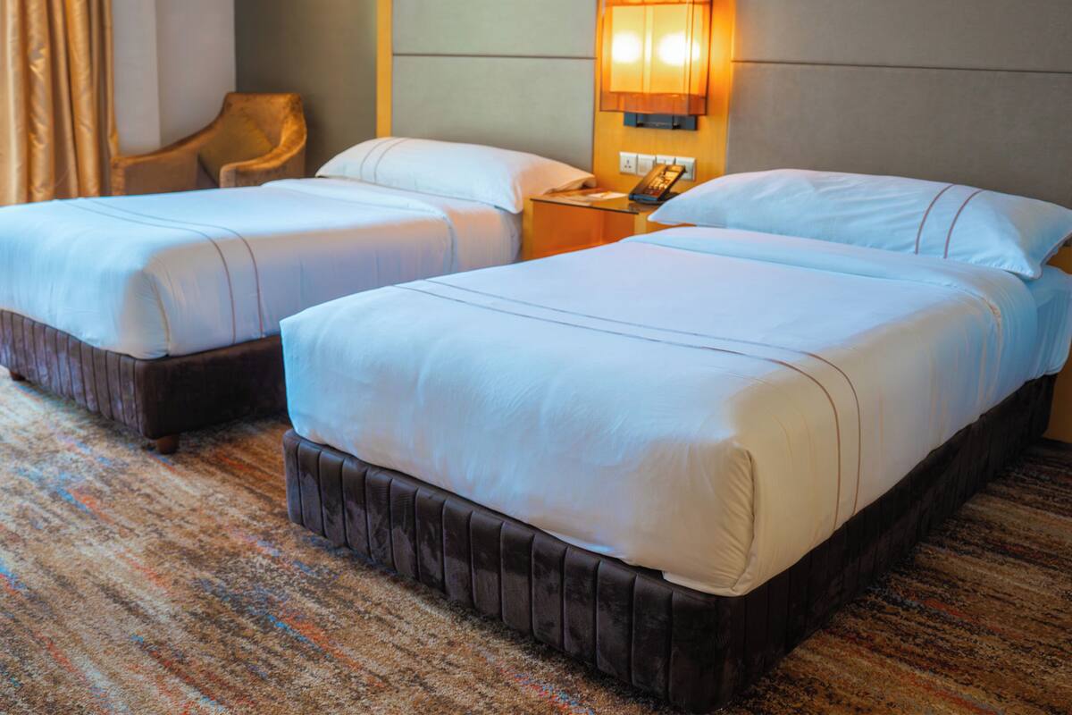 A hotel room with two beds, a nightstand with a lamp, and a chair.