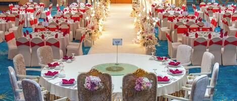 A banquet hall with round tables, white chairs with red sashes, and floral decorations.