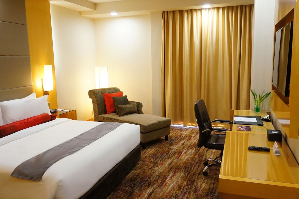 A hotel room with a large bed, a desk with a chair, a television, and a window with curtains.