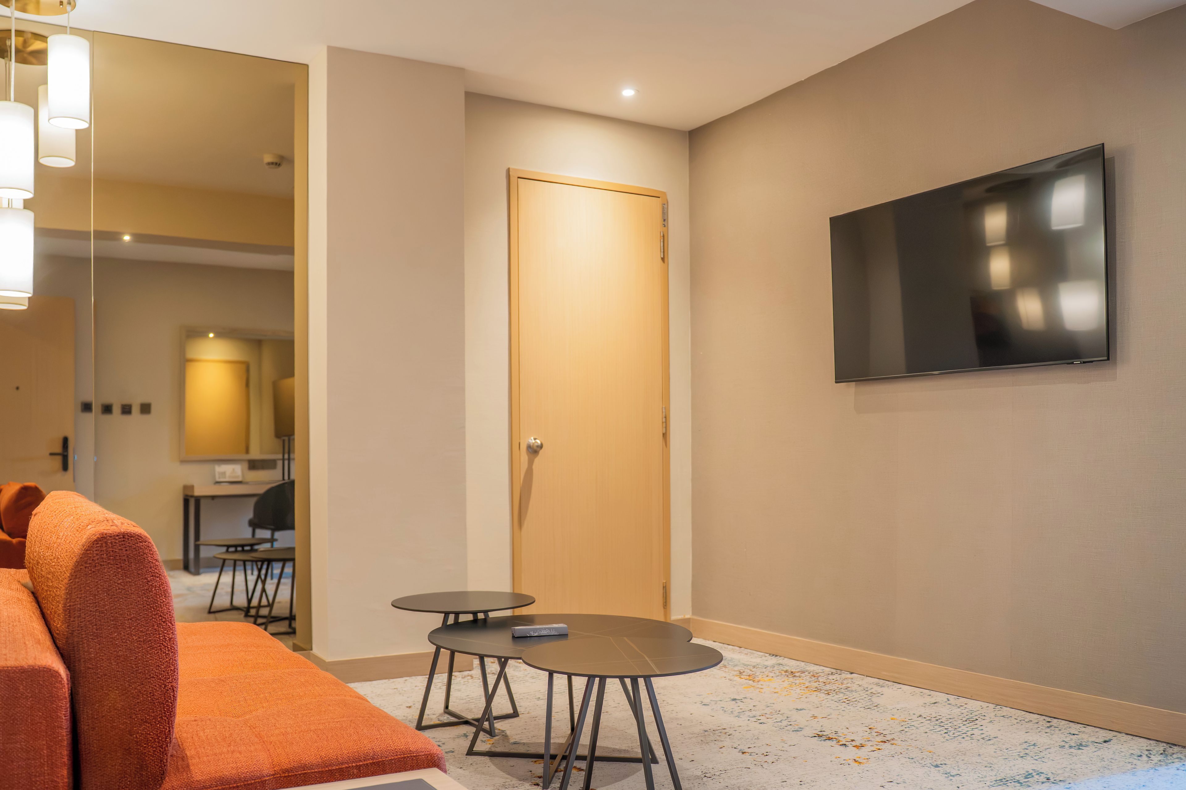 A hotel room with a sofa, a small table, a TV mounted on the wall, and a door.