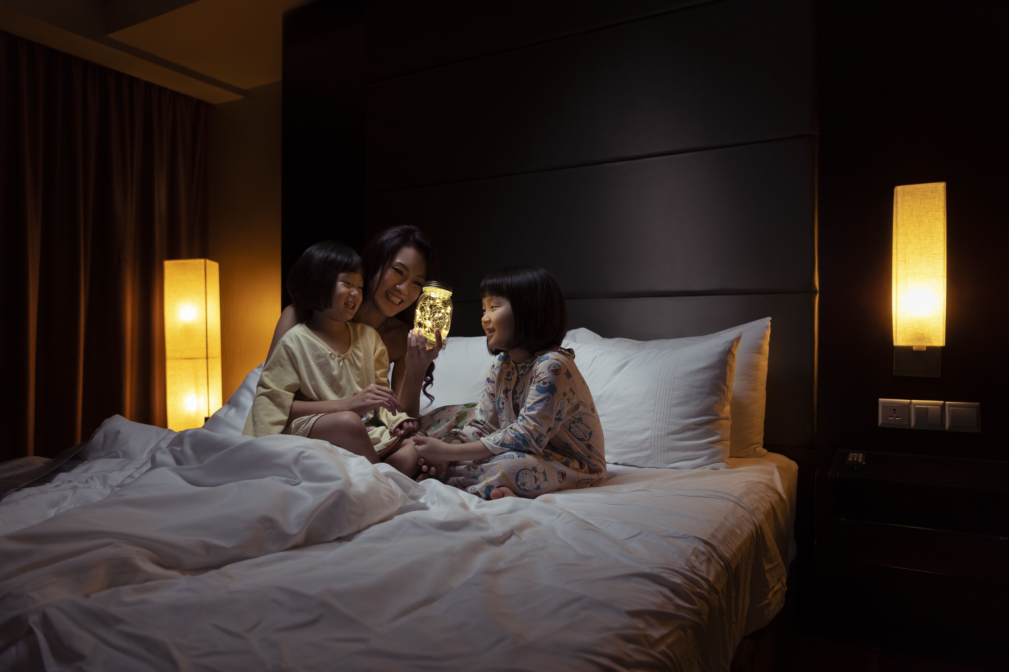 Una habitación de hotel con cama, mesita de noche y lámpara de pared.