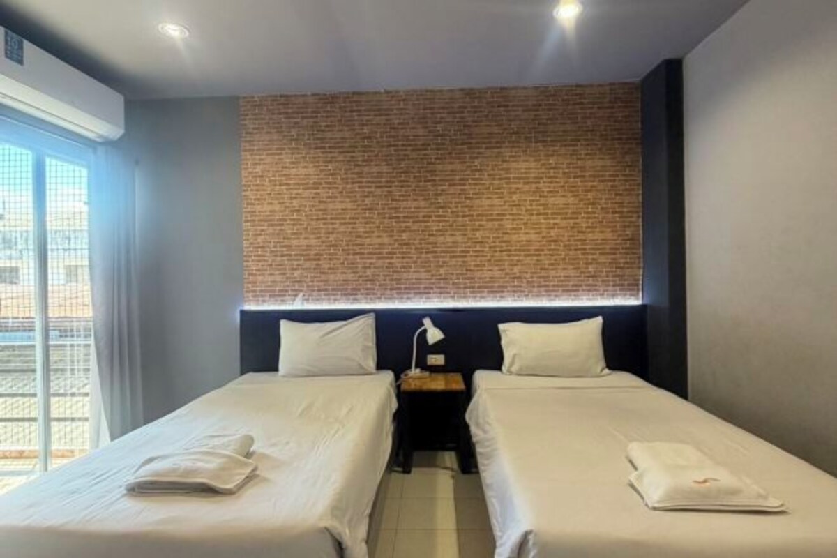 Une chambre d’hôtel avec deux lits, un mur décoratif en briques et une fenêtre avec des stores.