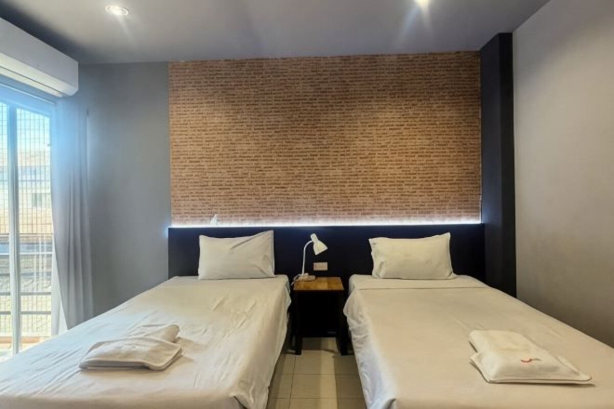Habitación de hotel con dos camas, una pared de ladrillo decorativa, una mesita de noche y un ventanal.