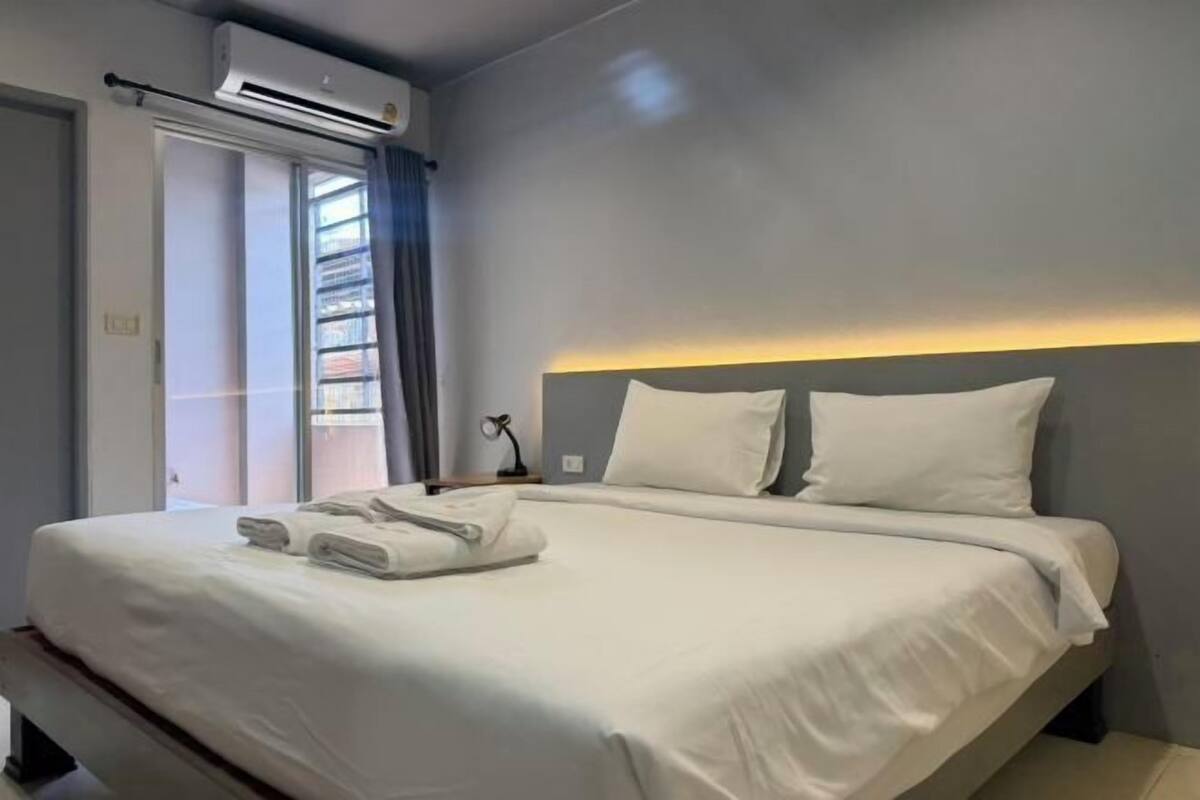 Ein Hotelzimmer mit Bett, Nachttisch, Klimaanlage, Fenster mit Blick und Vorhang.