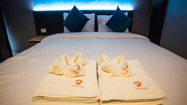 Een hotelkamer met een net opgemaakt bed, twee handdoeken met een logo en een hoofdbord met blauw verlichting.