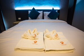 Une chambre d’hôtel avec un lit parfaitement fait, deux serviettes ornées d’un logo et une tête de lit dotée d’un éclairage bleu.