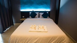 Een hotelkamer met een groot bed, twee kussens, een nachtkastje en een muur met blauw licht.