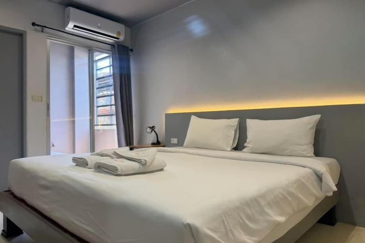 Une chambre d’hôtel avec un lit, une table de chevet, un appareil de climatisation, une fenêtre donnant sur un paysage agréable et un rideau.