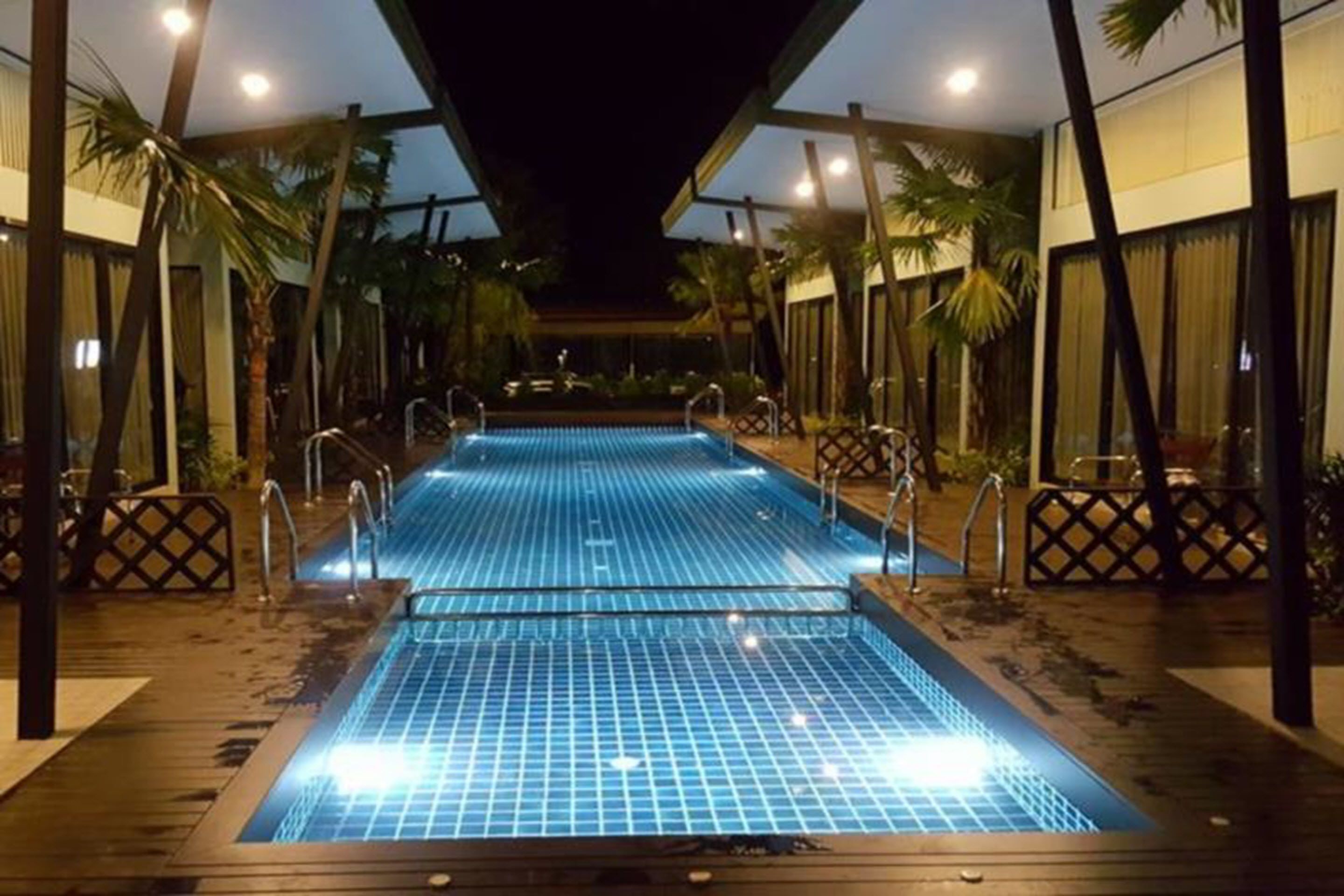 A pool area with two swimming pools, surrounded by palm trees and shaded by a covered walkway.