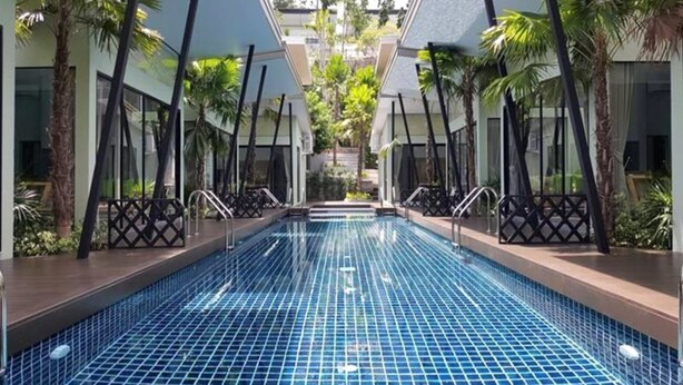 Una piscina interior moderna con suelo de baldosas, rodeada de palmeras y paredes de vidrio.