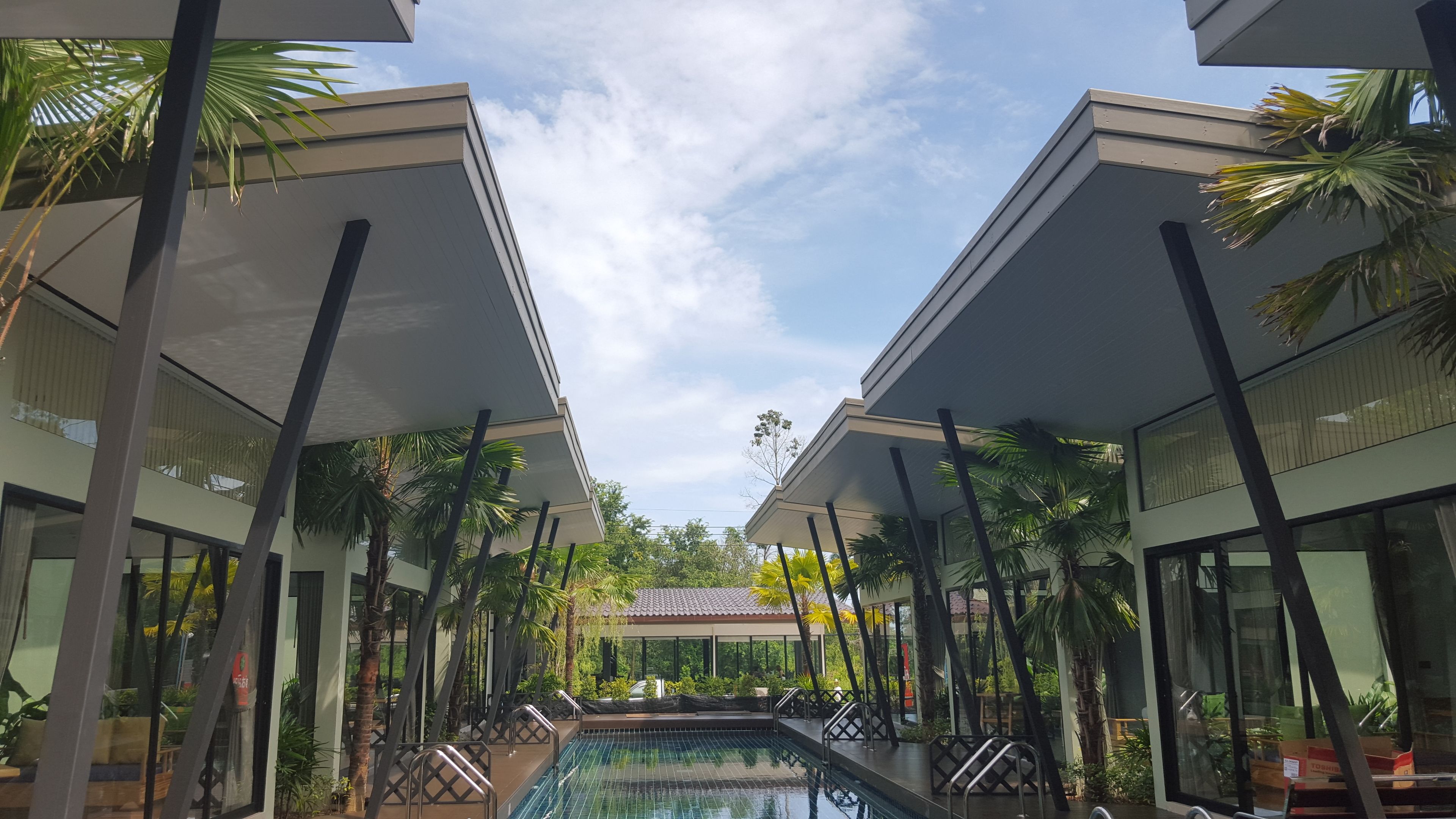 Un hotel moderno con una piscina central, rodeado de palmeras y paseos techados.