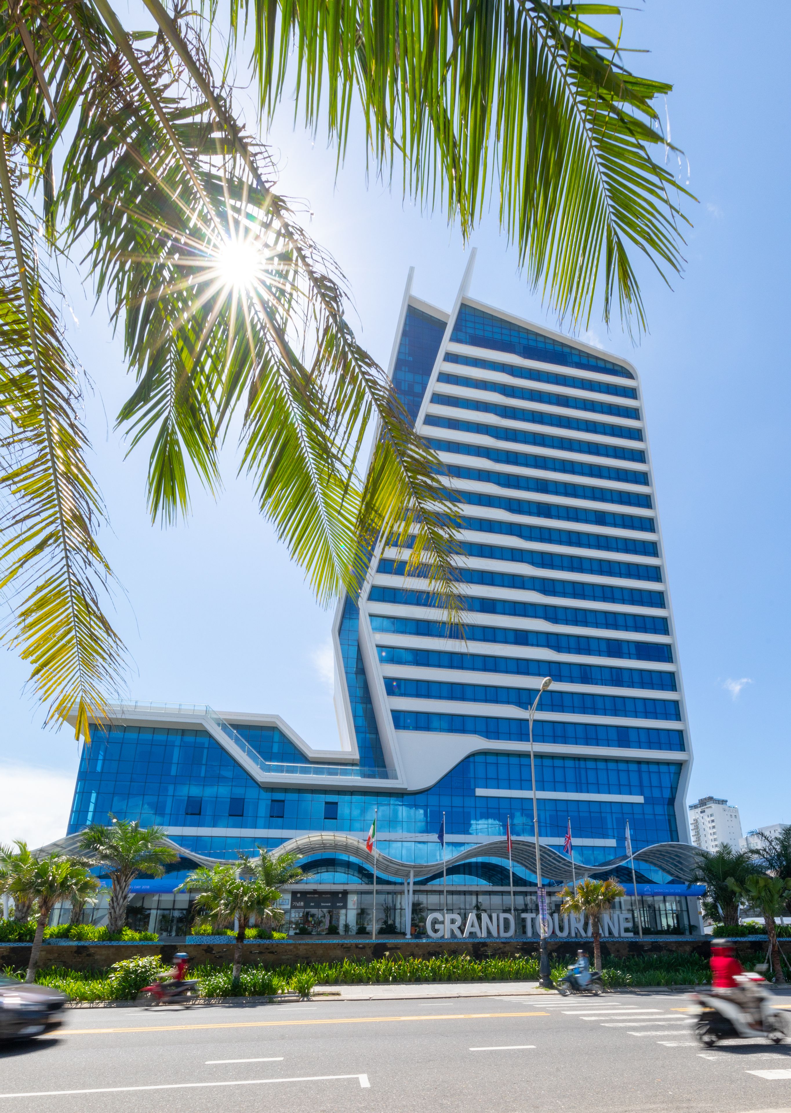 A modern hotel with a curved facade, large windows, and a prominent "GRAND TOURANE" sign.