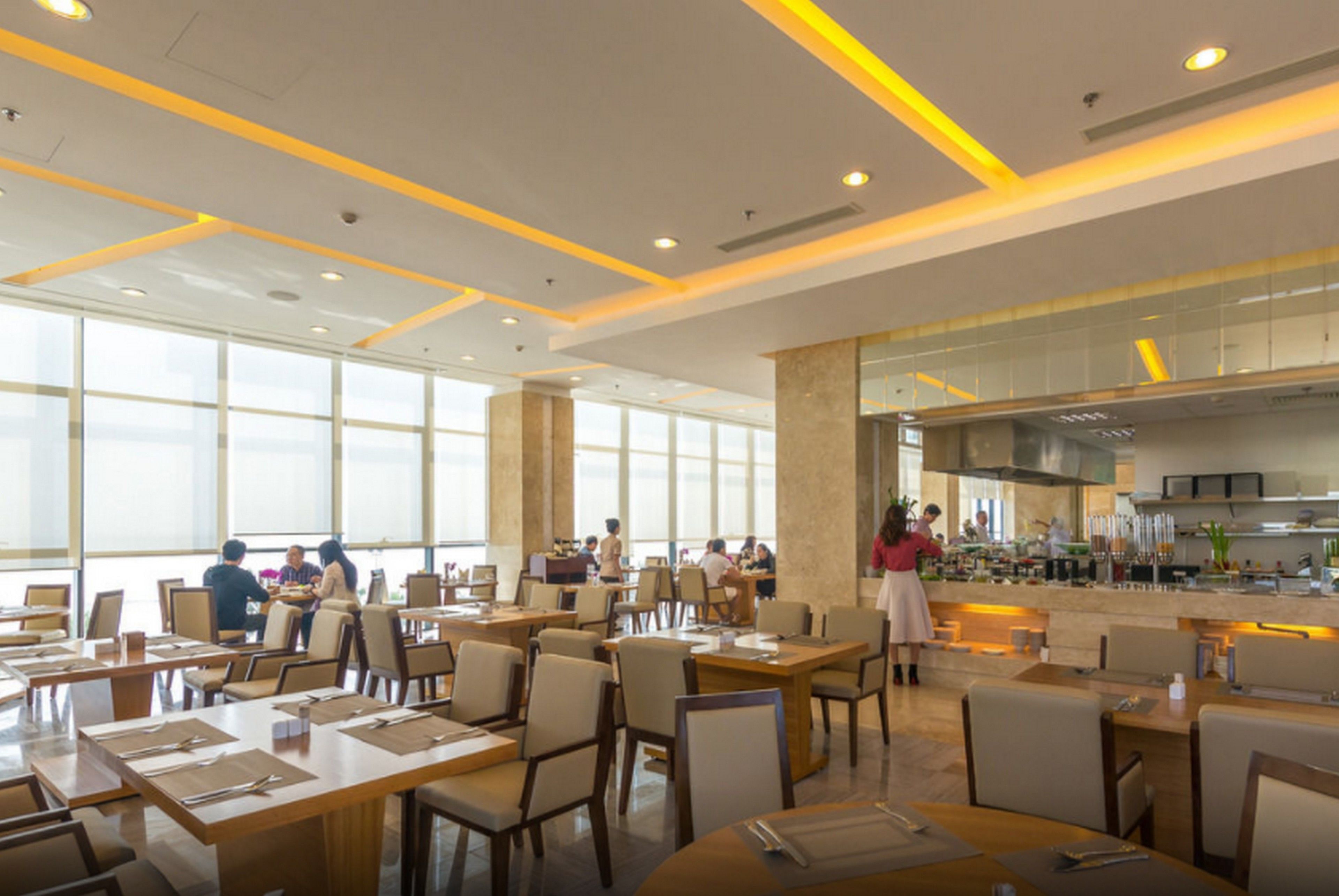 A spacious dining area with high ceilings, large windows, and a modern kitchen visible in the background.