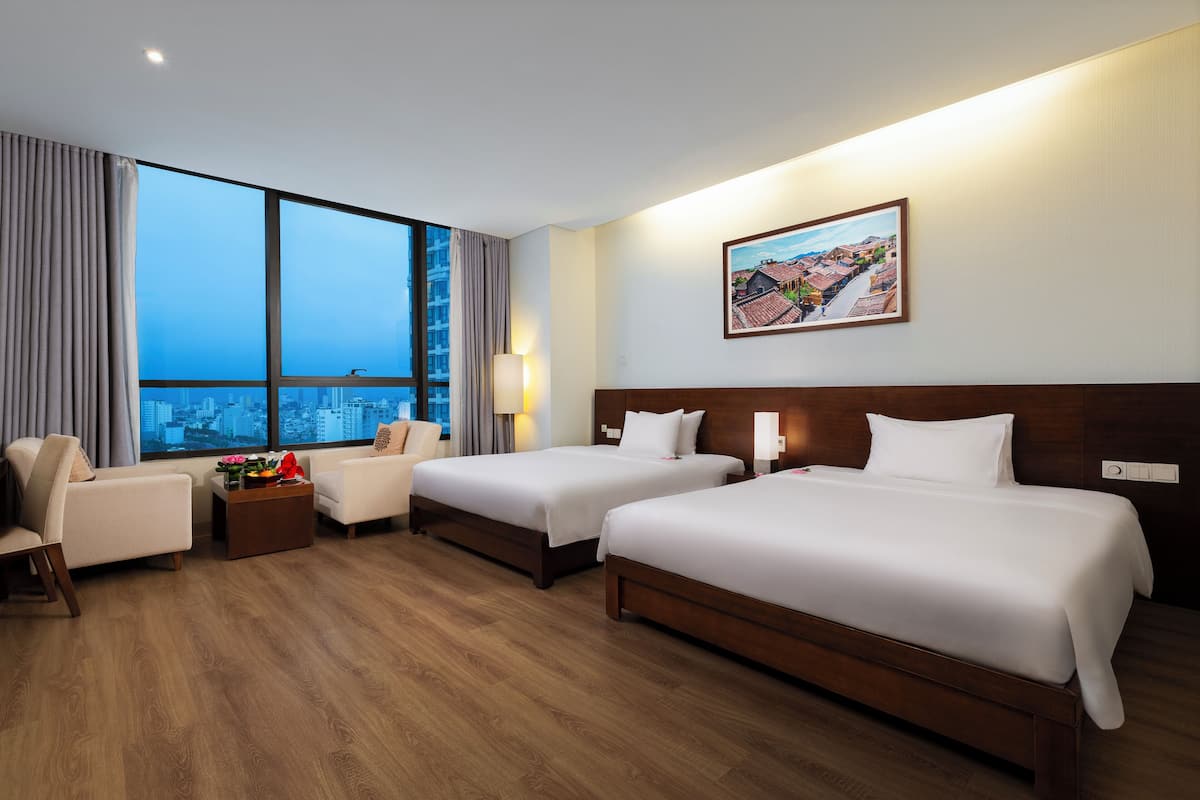 A hotel room with two beds, a sofa, a coffee table with flowers, a city view, and a painting on the wall.